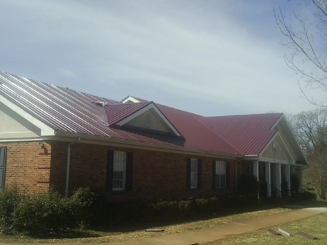 Red metal roof with gabled entries on a long brick building, from a Hail Damage Roof Repair job in Parsonsburg