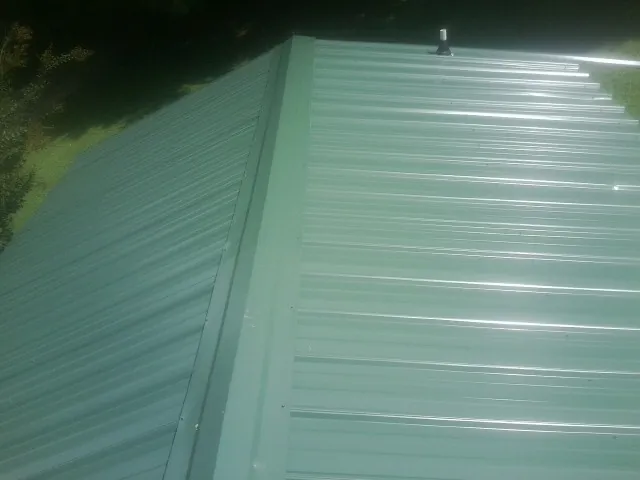 New green metal panels meeting at the ridge of a roof — Flat Roof Repair work by our crew in Parsonsburg