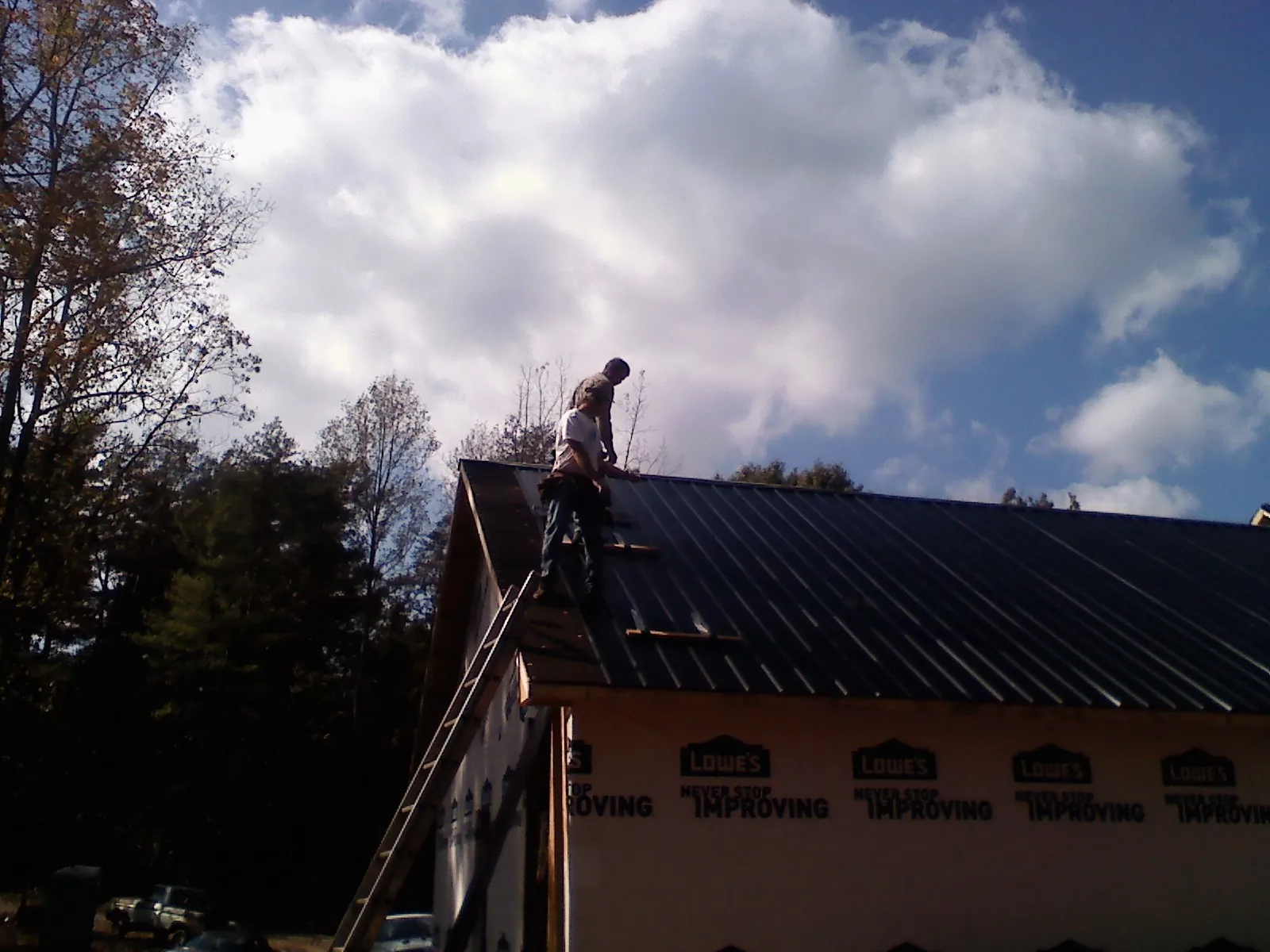 Roofer fastening dark metal panels high against a cloudy sky, from a Roof Inspection job in Parsonsburg
