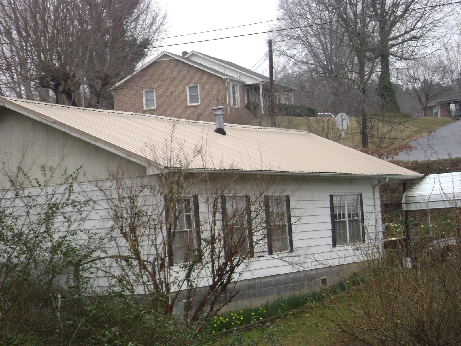Tan metal roof on a white sided house set into a hillside — Commercial Roofing by Roofing Brothers in Parsonsburg